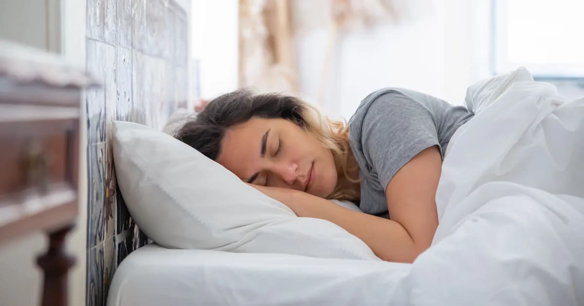 Mulher dormindo de lado com a cabeça apoiada em um travesseiro branco